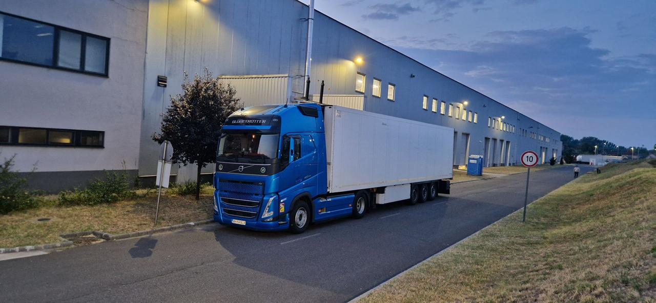 Semiremorcă albă și cap tractor albastru parcate lângă sediul Galexpres la apus.