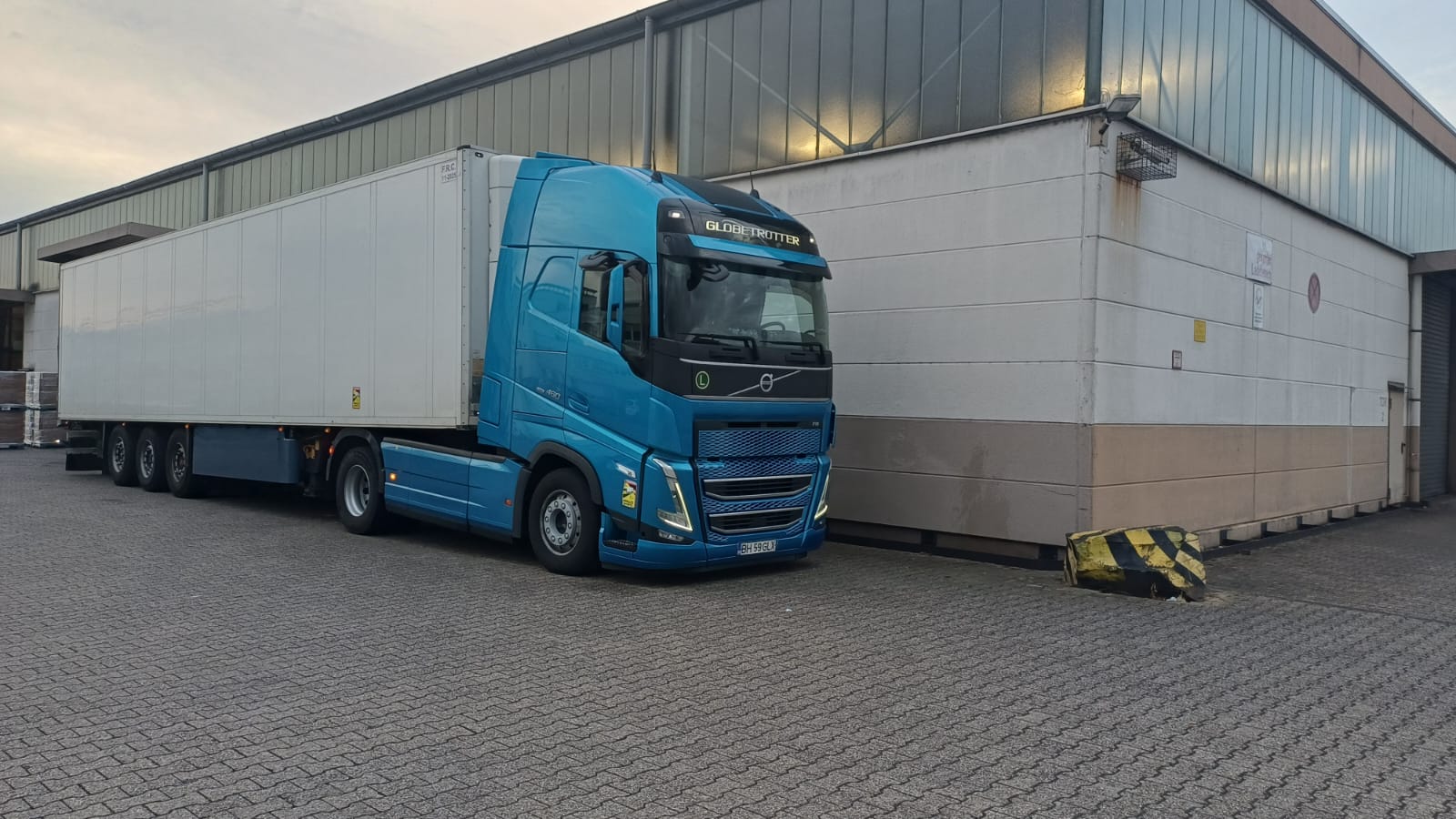 Cap tractor Volvo albastru, cu semiremorcă albă, parcat într-un parc industrial.