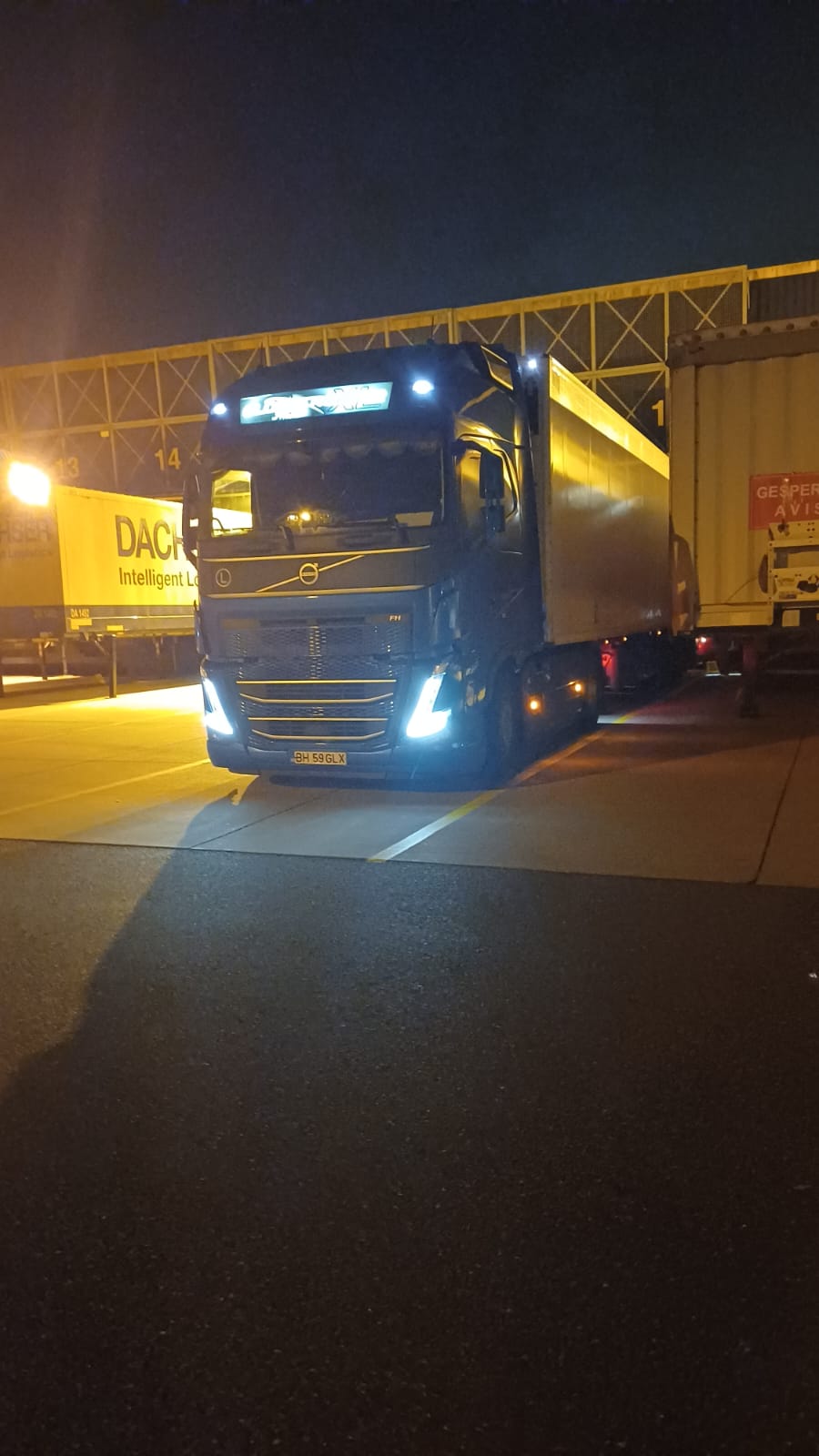 Camion albastru la docul de încărcare pe timp de noapte, luminat de proiectoare.